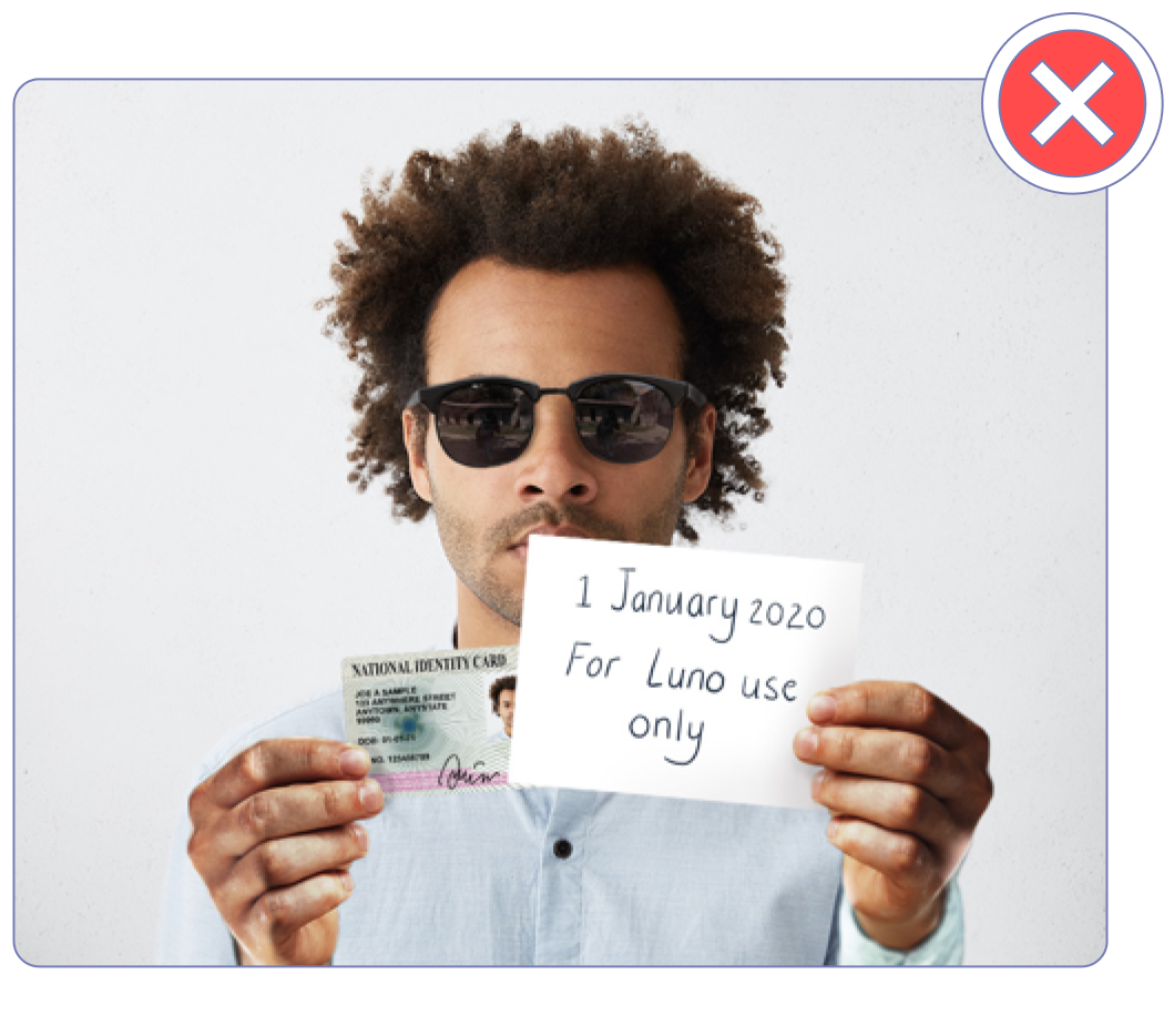 A selfie of a person wearing sunglasses and covering their ID with the note